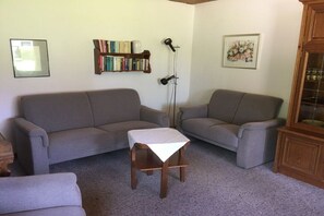 Sala de estar com dois sofás, uma mesa de madeira pequena, uma estante e um quadro na parede.
