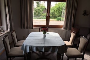 Ein Essbereich mit Tisch für vier Personen, einer Blumenvase und Blick auf Grünfläche.