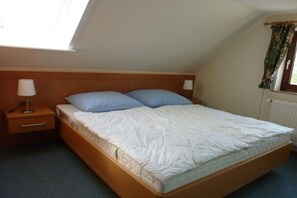 Ein Einzelbett mit Holz Kopfteil, ein Nachttisch mit Lampe und ein Fenster mit Vorhängen.