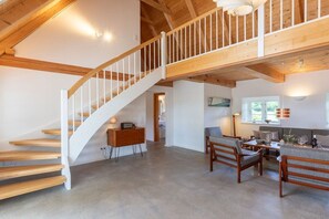 A spacious living area with a wooden staircase, a sofa set, and a dining table. - Holiday home with 3 bedrooms (Mittelangeln OT Havetoftloit)