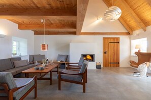 Ein geräumiges Wohnzimmer mit hoher Decke, Holzbalken, Kamin und moderner Möblierung.