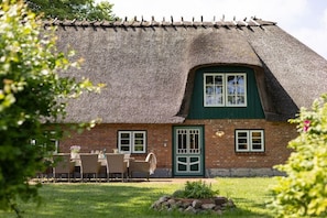 Ein traditionelles Haus mit Strohdach, rotem Backsteinhaus, einer grünen Tür und einem Essbereich mit Gartenmöbeln.