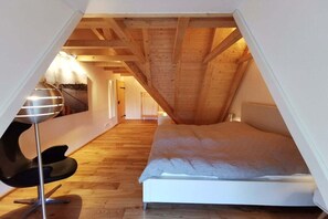 Ein Schlafzimmer mit geneigter Decke, einem Bett, einem modernen Sessel und einer Lampe.