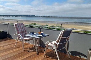 A balcony with a table and two chairs, overlooking a beach and water. - Holiday apartment with 2 bedrooms (Wittdün auf Amrum)