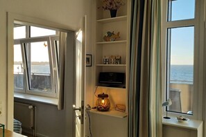A room with a view of the sea through a window, a shelf with decorative items, and a small table with a bird figurine. - Holiday apartment with 2 bedrooms (Wittdün auf Amrum)