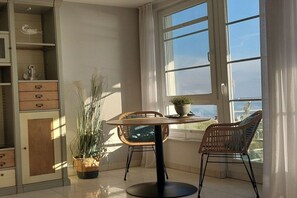 Ein Zimmer mit einem Esstisch, zwei Stühlen, einer Topfpflanze und Blick durch ein Fenster.