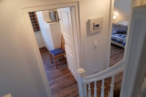 A room with a bed, a chair, a small table, and a door leading to another room. - Holiday home with 2 bedrooms (Wyk auf Föhr)
