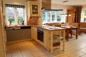 A kitchen with a dishwasher, oven, and a dining area with wicker chairs. - Holiday home with 2 bedrooms (Wyk auf Föhr)