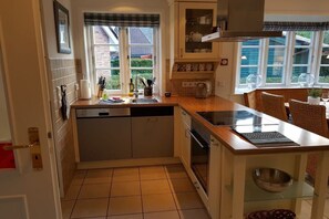 Een functionele keuken met een vaatwasser, een inbouwoven, een kookeiland met glazen blad en een raam met uitzicht.
