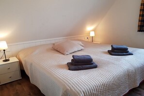 Ein Einzelbett mit gesteppter Bettdecke, zwei Nachttische mit Lampen und gefaltete Handtücher auf dem Bett.