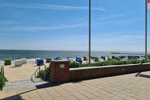 Eine Uferpromenade mit einer Backsteinmauer, Treppen, die zum Strand führen, und einer Reihe von blau-weißen Strandstühlen.