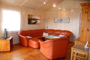 A cozy living room with a large orange leather sectional sofa, a wooden coffee table, and a television on a wooden stand. - Holiday home with 2 bedrooms (Otterndorf)