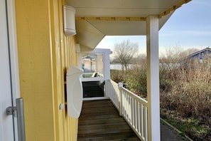 A wooden deck with a white railing, leading to a covered porch area. - Holiday home with 2 bedrooms (Otterndorf)