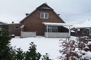 Ein Ziegelhaus mit überdachter Terrasse und einem mit Schnee bedeckten Rasen.