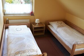 Ein kleines Zimmer mit zwei Einzelbetten, einem Fenster mit Blick, einem Nachttisch mit Lampe und einer Heizung.