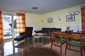 Ein Wohnzimmer mit einer Couch, einem Esstisch mit Stühlen, einem kleinen Couchtisch und einem Sessel mit Kissen.