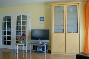 A living room with a television on a stand, a cabinet with glass doors, and a door with glass panels. - Holiday apartment with 1 bedroom (Ostseebad Baabe)