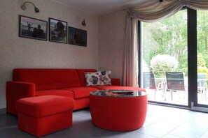 A red sofa, a glass coffee table, and a large window with curtains. - in the Stolkos holiday home (Trassenheide)