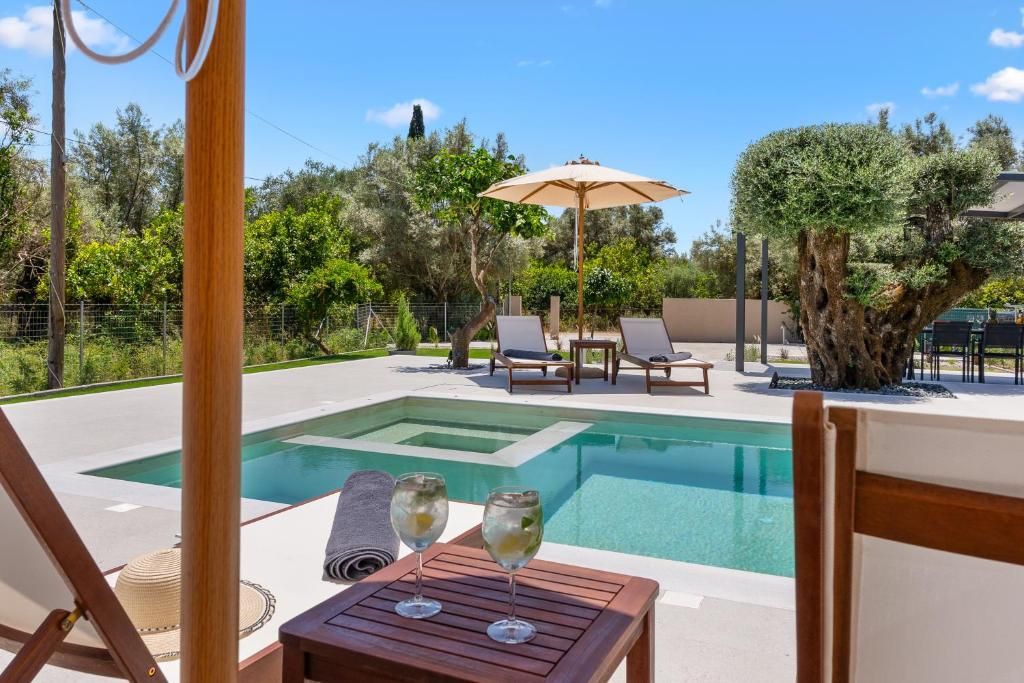 A pool area with lounge chairs and a table, surrounded by trees and a clear sky.