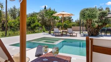 A pool area with lounge chairs and a table, surrounded by trees and a clear sky.