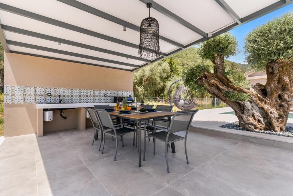 An outdoor dining area with a table and chairs, a hanging light fixture, and a large tree.
