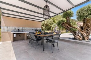 Un espacio de comedor al aire libre con una mesa, sillas, una lámpara colgante y un árbol grande.