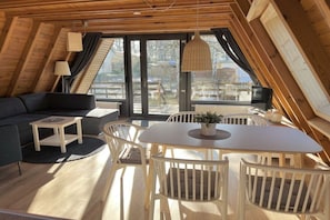 Ein gemütliches Loft-Zimmer mit Essbereich, einer Couch und einem großen Fenster mit Blick ins Freie.