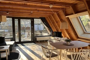 Ein modernes Interieur mit Essbereich, Fernseher und großen Fenstern, die einen Ausblick nach draußen bieten.