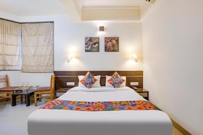 Una habitación de hotel con cama, dos lámparas de pared, un ventanal con cortinas y una pequeña mesa con sillas.