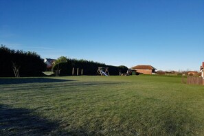 A grassy outdoor area with a swing set and a building in the background. - Barendorf Beach Suite (Barendorf)