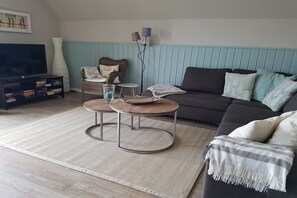 A living room with a sofa, a coffee table, a television, and a bookshelf. - Barendorf Beach Suite (Barendorf)