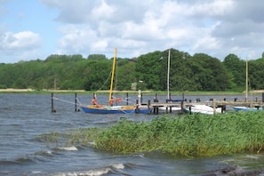 A calm lake with boats docked at a pier, surrounded by dense greenery. - Winningmay - Magnolia (Schaalby)