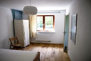 A bedroom with a bed, a chair, a window with curtains, and a radiator. - Winningmay - Magnolia (Schaalby)