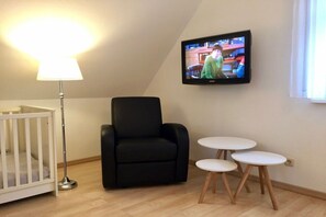 A room with a crib, a black armchair, and a TV mounted on the wall. - Holiday home with 2 bedrooms (Ostseeheilbad Zingst)