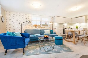 A modern living room with a blue sofa, a glass coffee table, and a dining area with a wooden table and chairs. - Holiday apartment Vogelhaus (Binz)