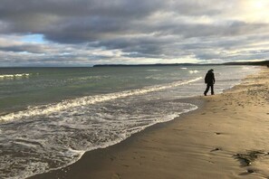 Een strand met een persoon die op het zand staat, golven naderen de kust, en een bewolkte lucht.