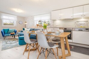 Een moderne keuken met witte kasten, een eethoek met een houten tafel en stoelen, en een zithoek met een blauwe bank en een glazen salontafel.