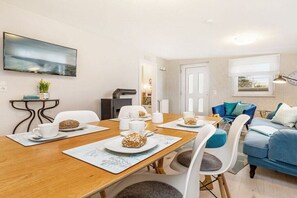 A modern living room with a blue sofa, a dining table with white chairs, and a flat-screen TV mounted on the wall. - Holiday apartment Vogelhaus (Binz)