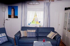 Ein Wohnzimmer mit einer Couch, zwei Sesseln, einem Tisch mit einem Glas und einer Lampe.