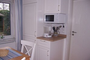 Eine Küche mit weißen Schränken, einer Mikrowelle, einer Kaffeemaschine und einem Fenster mit Blick auf Grünflächen.