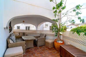 A covered outdoor seating area with wicker furniture, a potted tree, and a view of the surrounding buildings. - House in Nerja Near Playa Burriana Beach (Nerja)