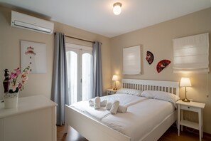 A hotel room with a bed, bedside tables, a nightstand, an air conditioning unit, a window with curtains, and wall decorations. - House in Nerja Near Playa Burriana Beach (Nerja)