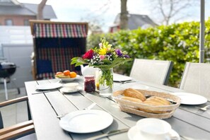 An outdoor dining table with plates, cups, a basket of bread, and a floral centerpiece. - Mühlenpark 1 W 3.10 "Klönschnack" (Prerow)