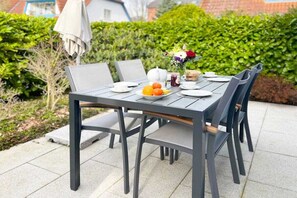 An outdoor dining table with chairs, a vase of flowers, and a plate of fruit. - Mühlenpark 1 W 3.10 "Klönschnack" (Prerow)