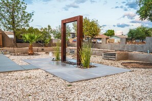A landscaped outdoor area with a concrete pathway, gravel ground, and a wooden structure. - 11327 Desert Oasis with Year-Round Pool (Apache Junction)