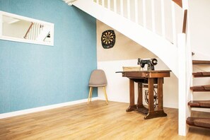 Ein Zimmer mit Holzboden, Dartscheibe, Nähmaschine, Stuhl und einer Treppe.