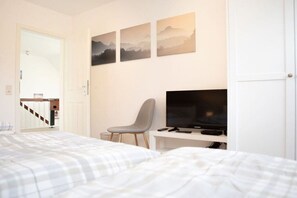Ein Schlafzimmer mit einem Bett, einem Schreibtisch mit Fernseher und einem Sessel. Darüber befinden sich drei Bilder an der Wand.