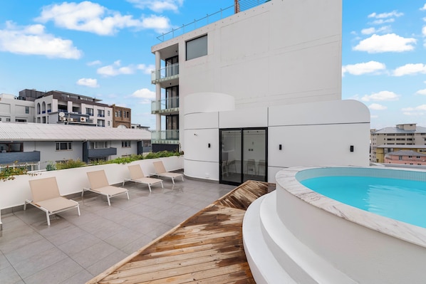 Un área de piscina en la azotea con sillones de descanso y una terraza de madera.
