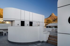 A modern building with a curved facade, a staircase leading to an upper level, and a view of a mountain in the background. - Apartments by Morea Sea Point (Cape Town)