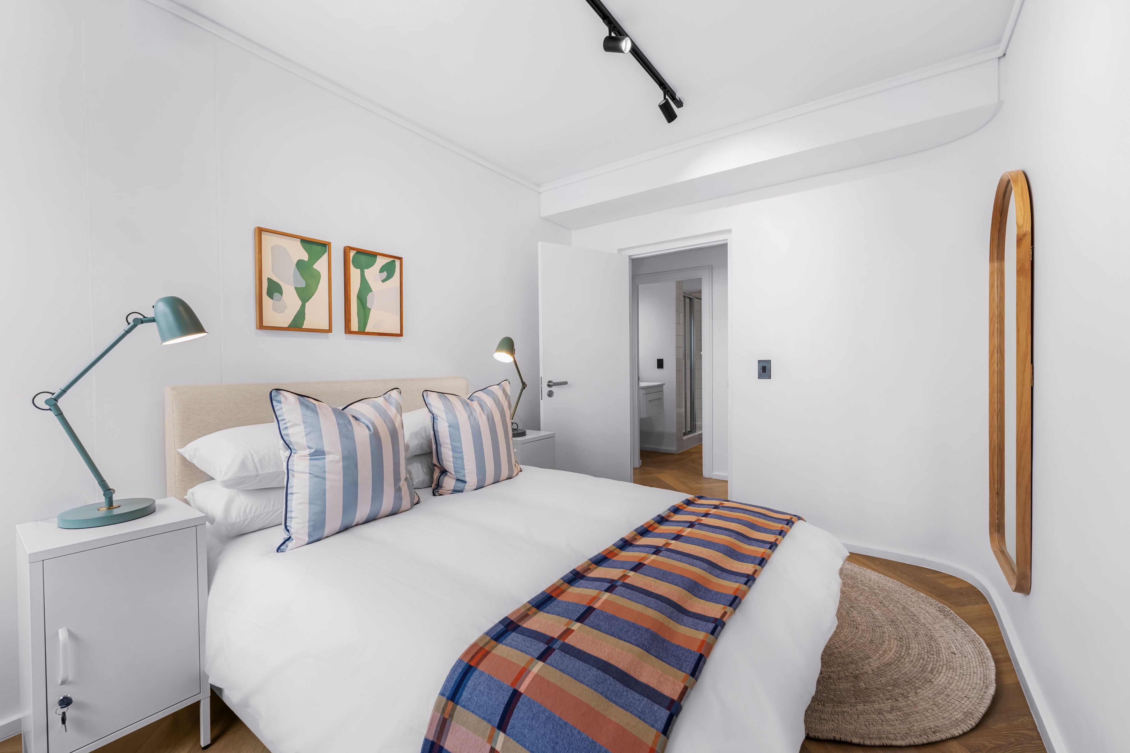 Un dormitorio moderno con cama, mesitas de noche, una lámpara de escritorio y un espejo.